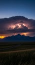 Lightning illuminates a dark, towering cumulus cloud over a mountain range during Royalty Free Stock Photo