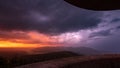 A lightning lights up the cloudy sky during a thunderstorm while the morning sun turns the horizon a deep orange Royalty Free Stock Photo