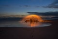 Lightpainted orb with flying sparks on a beach with a warm sunset in the background