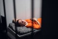 Lights out in prison. A convict in an orange robe rests on a bunk in a cell with a book. Royalty Free Stock Photo