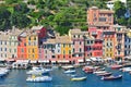 Liguria Portofino view of harbor with moored boats and pastel colored houses lining the bay with trees on hills behind, Italy.