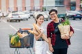 Likable asian couple hold paper eco bags with organic healthy food in hands while standing near store mall. Happy family Royalty Free Stock Photo