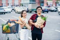 Likable asian couple hold paper eco bags with organic healthy food in hands while standing near store mall. Happy family