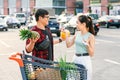 Likable asian couple standing near shopping cart,man holds pineapple and melon and beautiful woman counts the banknotes
