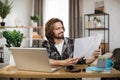 Likable young caucasian man sitting at desk with laptop and holding papers.