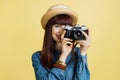 Likable young woman in jeans shirt and hat, covering face and taking pictures on retro vintage photo camera isolated on Royalty Free Stock Photo