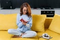 Likable young woman writing her personal notes into her diary while sitting in the modern stylish kitchen.