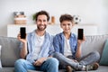 We like this app. Happy father and son showing their smartphones with blank black screens, sitting on sofa at home Royalty Free Stock Photo