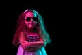 Stylish little girl, beginner fashion model wearing sunglasses posing isolated over dark background in neon light Royalty Free Stock Photo