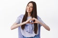 Like it. Smiling cute young woman showing heart gesture, tilt head and look adorable, I love you sign, standing against Royalty Free Stock Photo