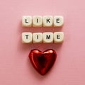 Like time words, made of wooden letters with red heart on pink background. Social media concept