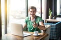 Like! Young happy businessman in green t-shirt sitting and working on laptop, looking at camera with thumbs up and toothy smile Royalty Free Stock Photo