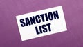 On a lilac background, a white card with the words SANCTION LIST