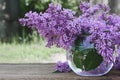 Lilac bouquet in a round glass vase on wooden table