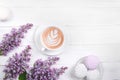 Lilac, coffee with latte art and marshmallow on white wooden table. Romantic morning. Flat lay