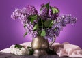 Lilac flowers in an old vase, near sprig of white flowers on background of fine fabric Royalty Free Stock Photo