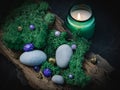 Lilac, golden stone lies in the bark of a tree with green moss, gray stones and a burning candle on a black Royalty Free Stock Photo