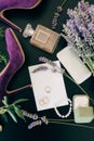 Lilac high heel shoes, a bottle of perfume, a smartphone, jewelry and flowers on a green background