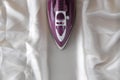 Lilac iron on a piece of white crumpled fabric. ironing clothes. household electrical appliances. view from above