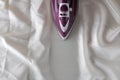 Lilac iron on a piece of white crumpled fabric. ironing clothes. household electrical appliances. view from above