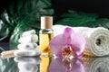 Lilac orchid flower, clear bottle of yellow oil, wooden sticks and towel with white stones and monstera on black surface Royalty Free Stock Photo