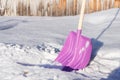 A lilac plastic shovel with a wooden handle stands in the fluffy white snow