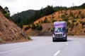 Lilac semi truck with trailer is moving along winding highway on Royalty Free Stock Photo