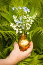 Lilies of the valley in May and forget-me-nots in a charming little jug held in a woman`s hand against the background of a garden