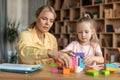 Liltle preschooler girl playing with wood blocks and teacher educador help, sitting at table in office Royalty Free Stock Photo
