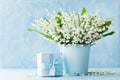 Lily of the valley flowers in blue vase and gift box on rustic table. Greeting card for woman day.