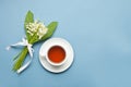 Lily of the valley flowers and cup of tea on blue background. Flat lay, top view, copy space Royalty Free Stock Photo