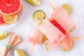 Lime and grapefruit popsicles, top view table scene over white marble