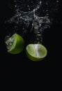 Lime green fruit that is falling and has water spreading with a black background