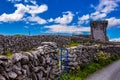 Limestone fences with a blue metal gate next to a country road on Inis Oirr Island with the ruined tower in the background