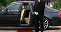 Limo driver standing next to opened car door with red carpet