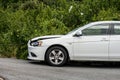 Crash damaged white car parked by a hedge..