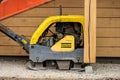Yellow Atlas Copco plate compactor by a house..