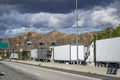 Line of big rig semi trucks with loaded semi trailers standing on the at the weighing station with scales for weighing along the