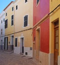 Line of brightly painted traditional houses on a cobbled quiet curved empty street in ciutadella menorca with wooden shutters an Royalty Free Stock Photo