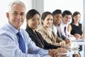 Line Of Business People Listening To Presentation Seated At Glass Boardroom Table Royalty Free Stock Photo