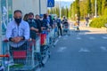 Line of customers outside of a local grocery store. In front a man with white sweater and black face mask for covid19.