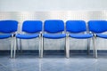 Line of empty blue visitor chairs standing near wall at reception or in bank