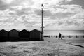 A line of four beach huts and a street lamp silhoutted black by the sun shining directly at the camera through a dramatic blue and