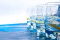 Line of Glasses of refreshing water with ice and lemon on a blue background. Heat concept, fresh. Natural light, copy space Royalty Free Stock Photo