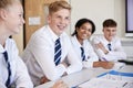 Line Of High School Students Wearing Uniform Sitting At Desk In Classroom