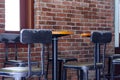 A line of industrial metal black chair stands beyond a long brown hard wood table at cafe or coffee shop interior with red brick Royalty Free Stock Photo