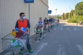 Man with glasses and surgical mask pushes his shopping cart, long line of customers outside the convenience store.buy goods for st