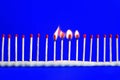 Line of red unused and four burning safety matches on blue