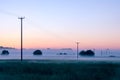 A line of telegraph poles heading into the distance across a field on a beautiful misty, summers morning, just before sunrise