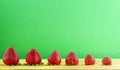 A line up of different sizes of ripe fresh strawberies on yellow and green background with copy space